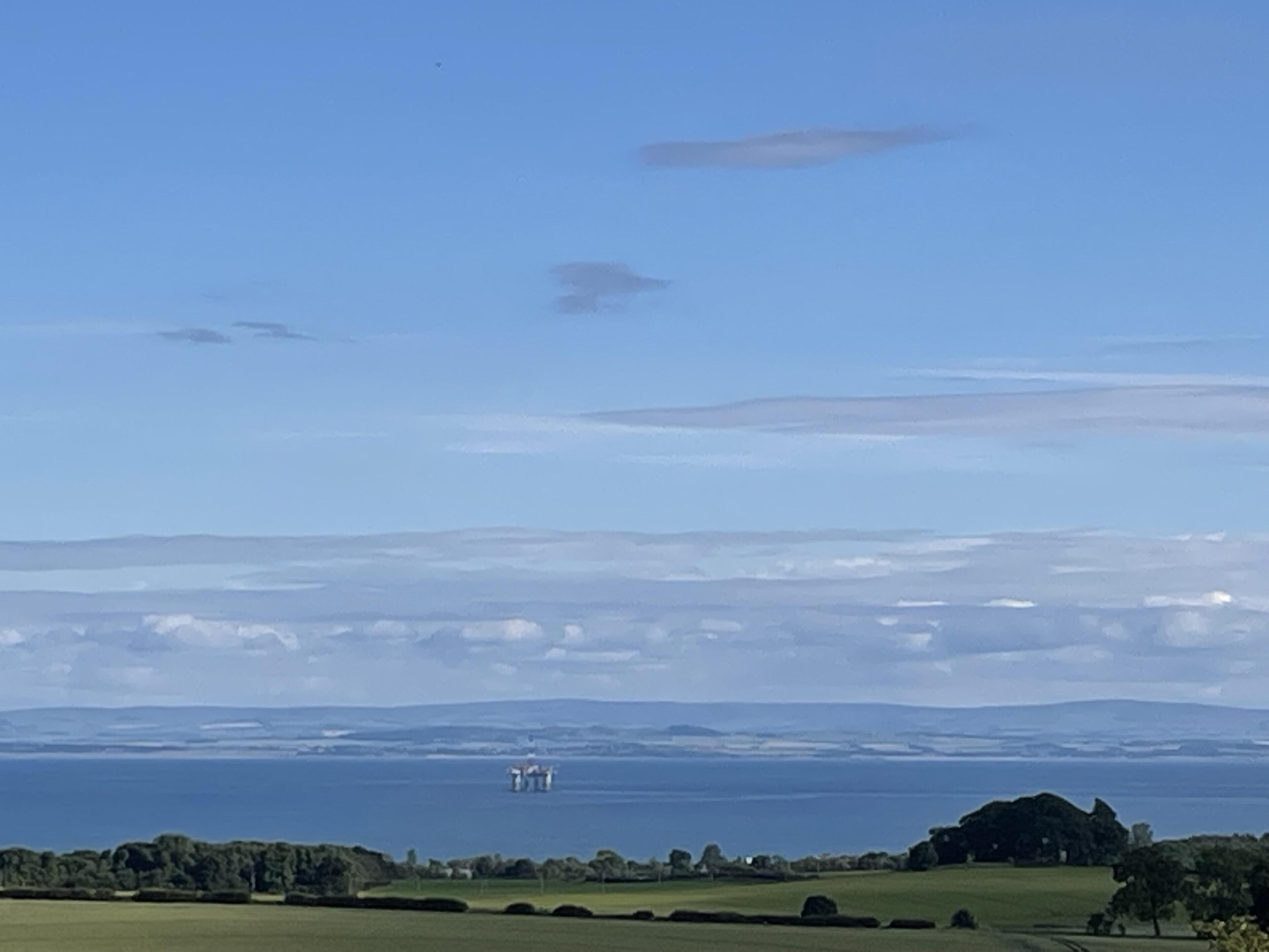 Paesaggio costiero con cielo sereno, acqua in lontananza e alcune strutture all'orizzonte.