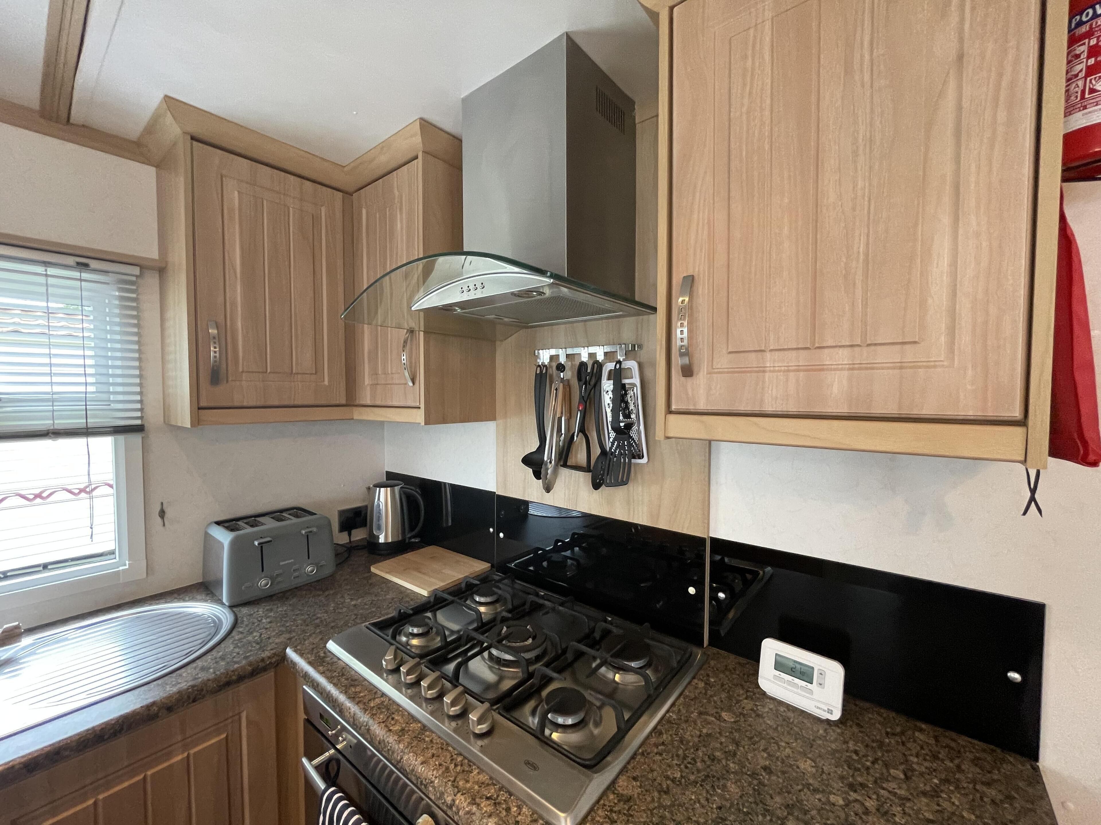 A compact kitchen with wooden cabinets, a gas stove, a toaster, and a kettle.