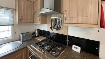 A compact kitchen with wooden cabinets, a gas stove, a toaster, and a kettle.
