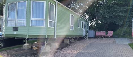 A green mobile home with a small porch and a gravel driveway.
