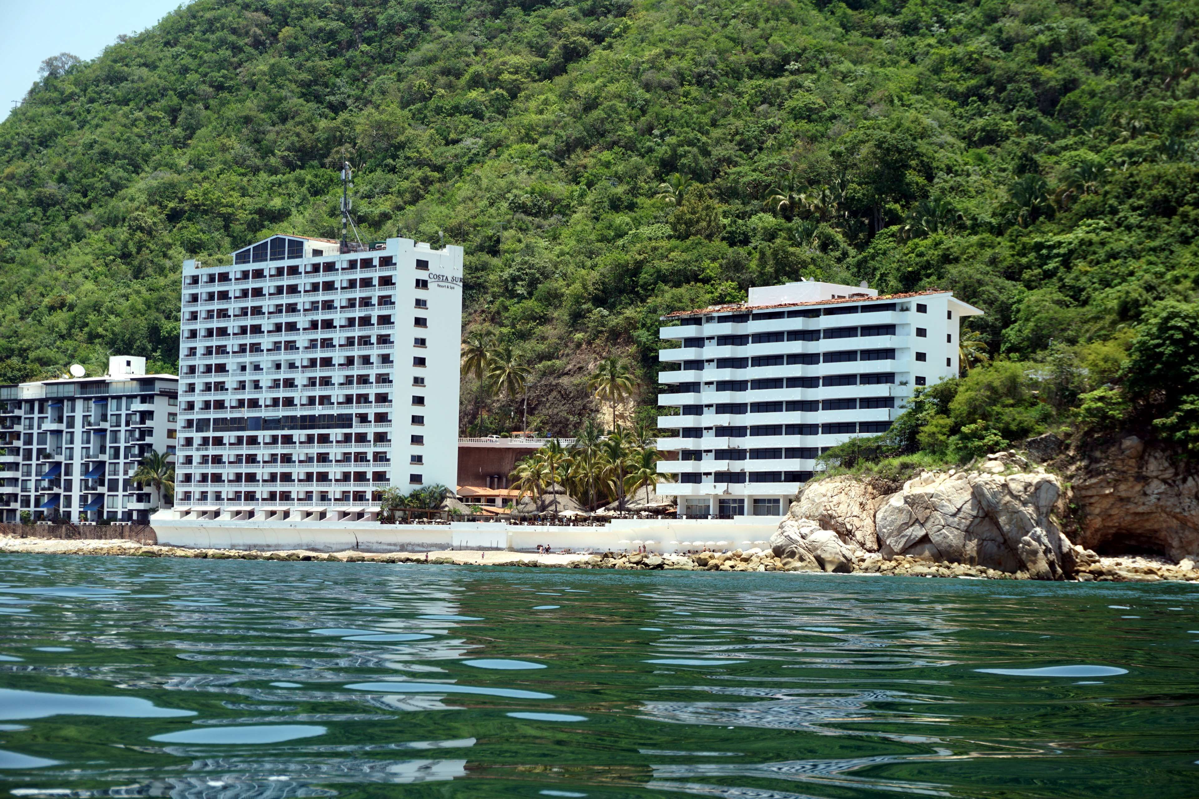 Un hôtel situé sur la côte, avec plusieurs étages, un rivage rocheux et une végétation luxuriante en arrière-plan.
