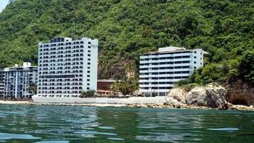 Un hôtel situé sur la côte, avec plusieurs étages, un rivage rocheux et une végétation luxuriante en arrière-plan.