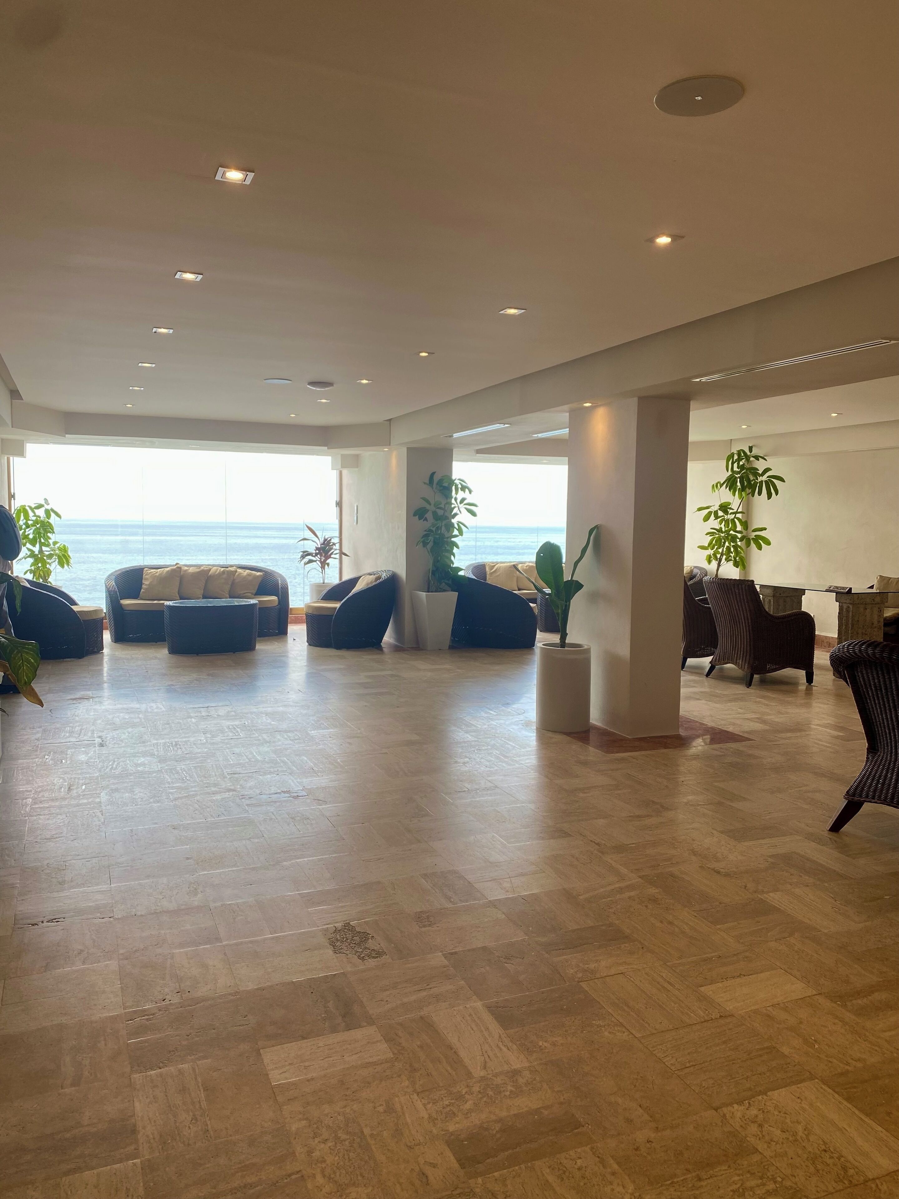 A spacious living area with a view of the sea, featuring multiple seating arrangements and potted plants.