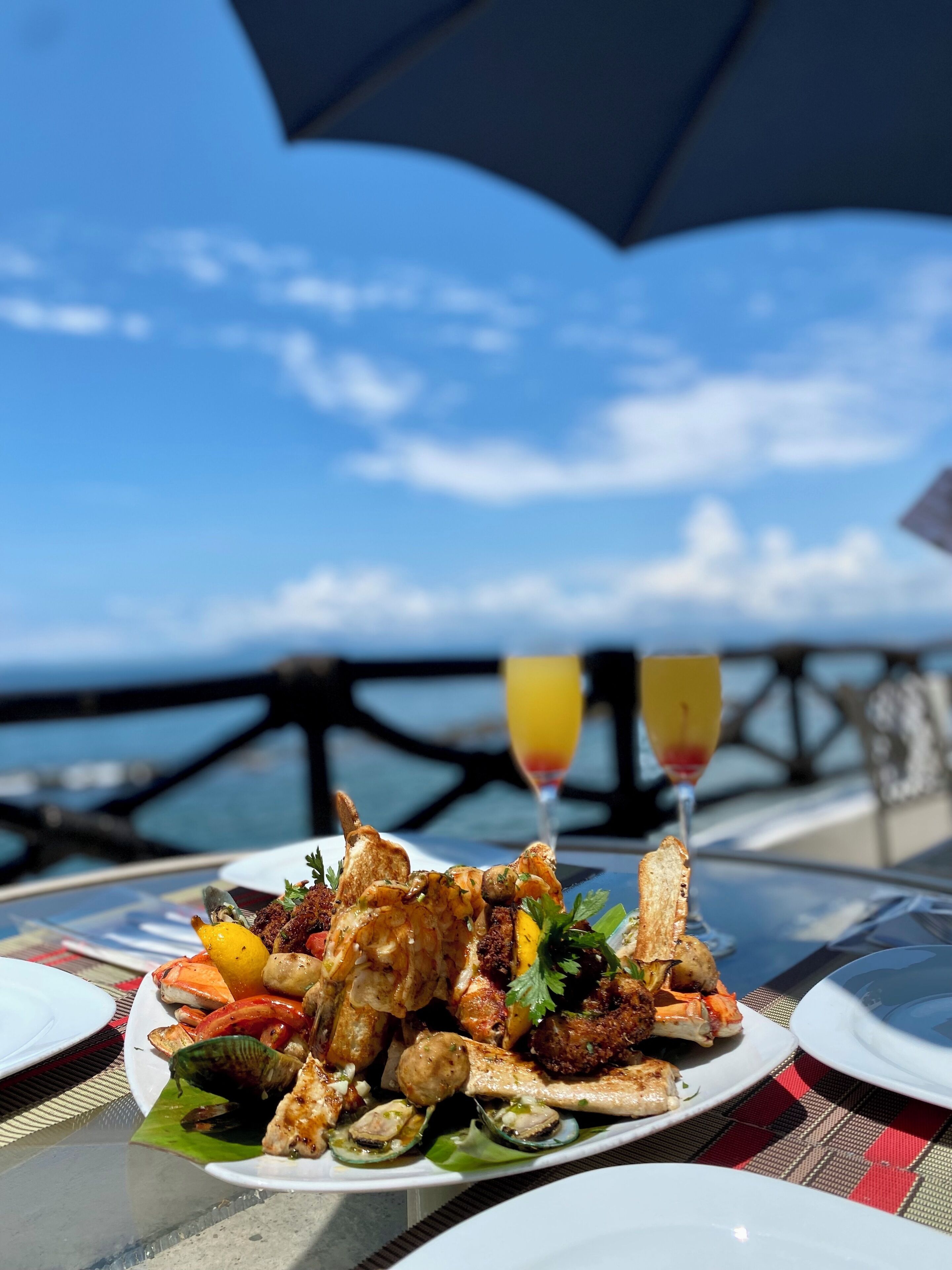 Ein Tisch mit einer Meeresfrüchteplatte, zwei Orangensaftgläsern und Blick auf das Meer.