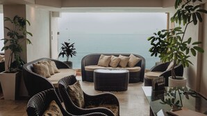 A modern living room with wicker furniture, a glass coffee table, and a view of the sea. - Costa Sur All Inclusive Classico Collection by Sonesta (Puerto Vallarta)
