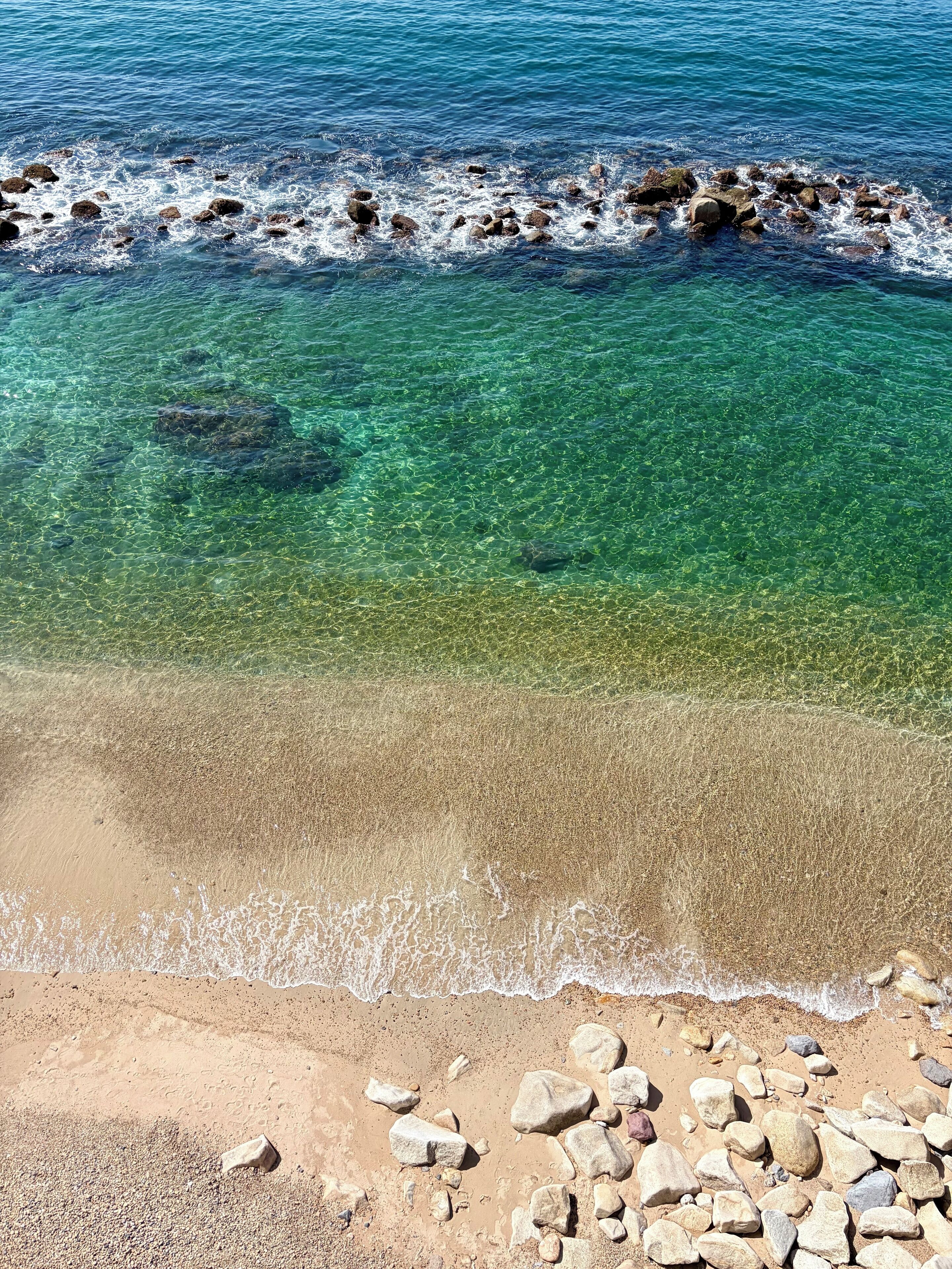 A beach with clear water, pebbles, and a rocky shoreline.