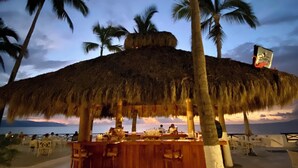A beachside bar with a thatched roof, palm trees, and a view of the ocean. - Costa Sur All Inclusive Classico Collection by Sonesta (Puerto Vallarta)
