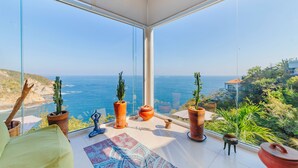 Habitación moderna con amplios ventanales y vistas al mar, con plantas en macetas y un tapete de yoga.