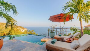 A poolside area with a lounge chair, a red umbrella, and a view of the ocean.