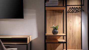 Een moderne kamer met een houten bureau, een stoel, een aan de muur bevestigde televisie en een houten wandplank met een hanggedeelte.