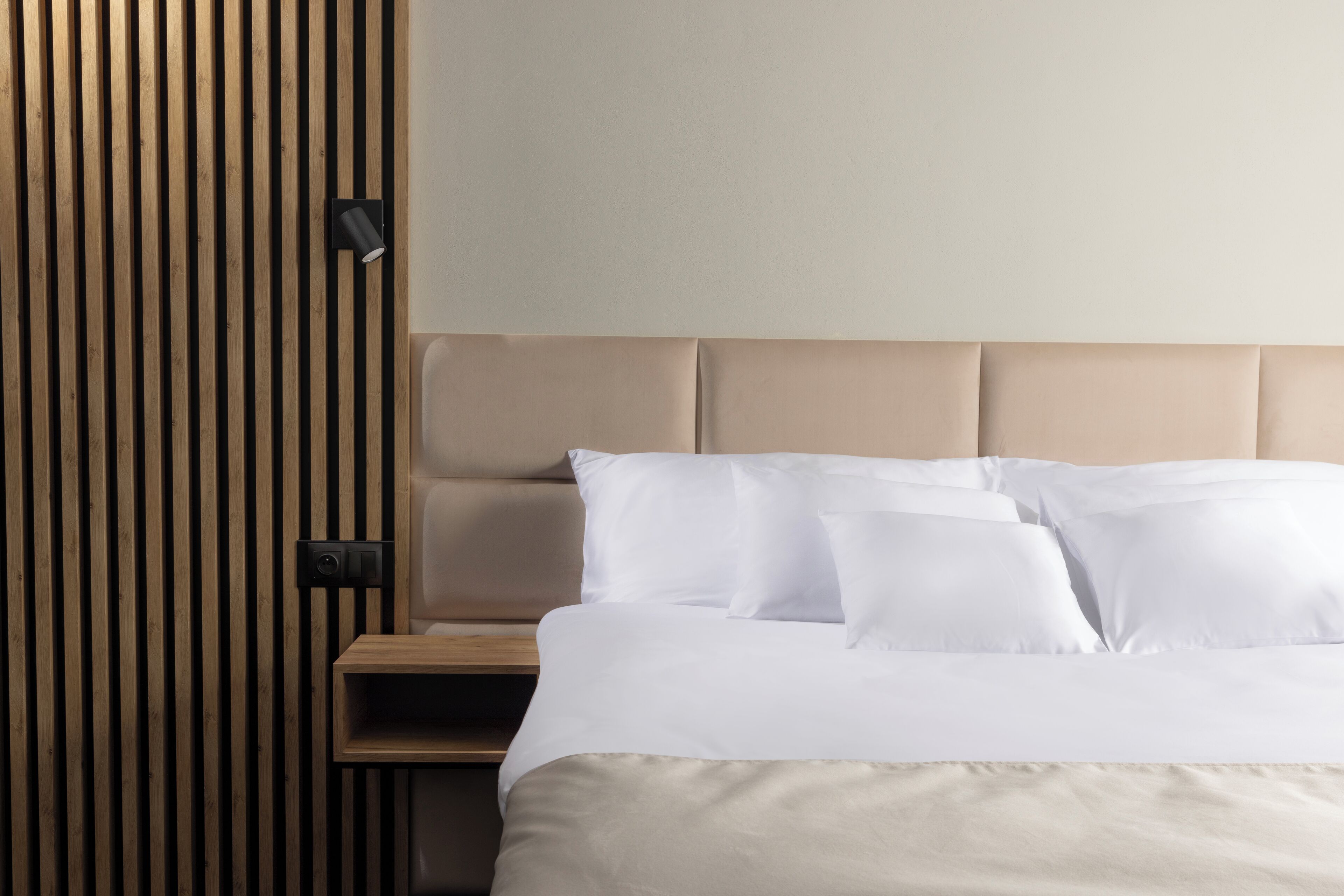 A neatly made bed with white linens and a wooden headboard.
