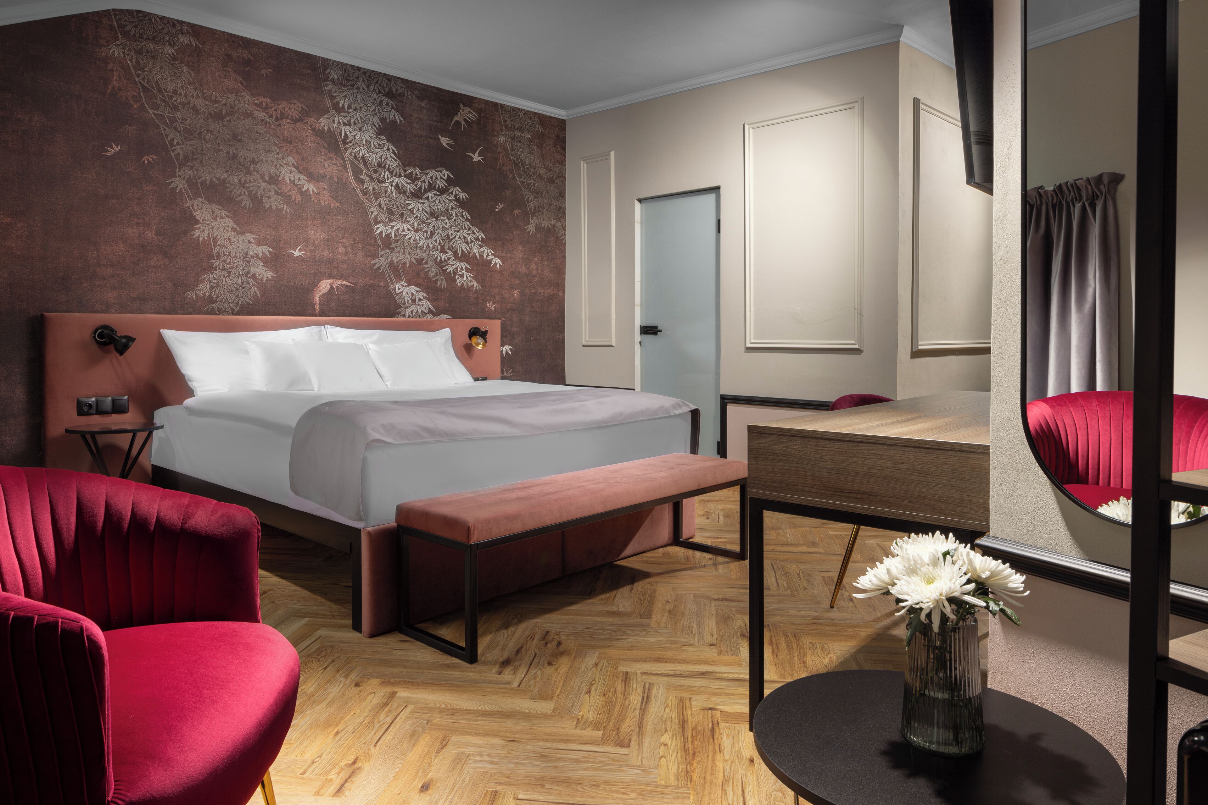 Une chambre d’hôtel avec un lit, un banc, un bureau, une chaise et un miroir.