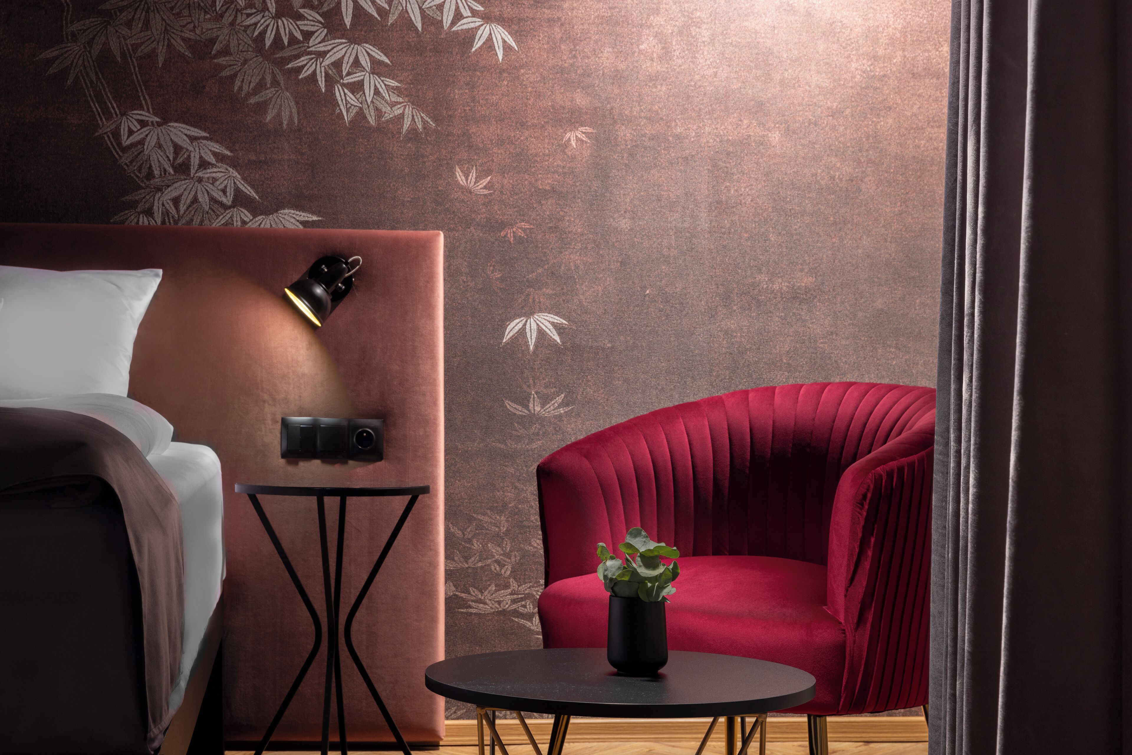 A modern room with a bed, a red armchair, a small table with a plant, and a wall with a bamboo leaf pattern.