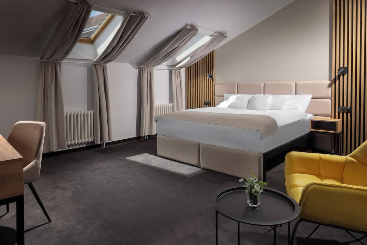A modern hotel room with a large bed, a desk, a chair, and a small table with a plant.
