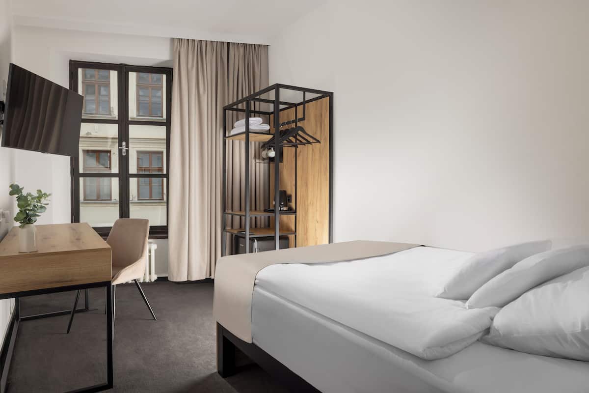 A hotel room with a bed, a desk, a chair, a wardrobe, and a window with curtains.