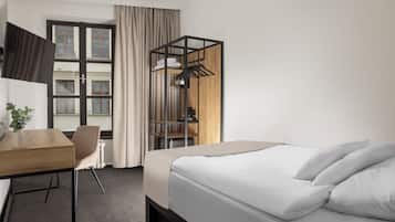 Habitación de hotel con cama, escritorio, silla, armario y ventana con cortinas.