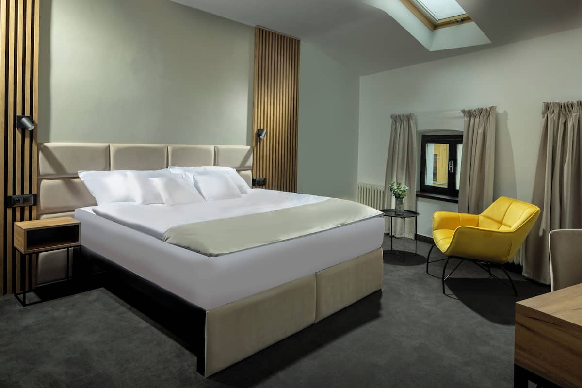 A modern hotel room with a large bed, a small table, a yellow armchair, and a skylight.