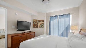 A hotel room with a bed, a TV on a wooden dresser, a painting on the wall, and a window with curtains.