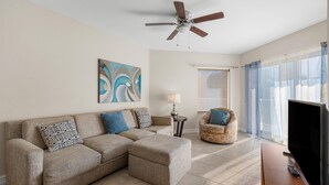 A living room with a sectional sofa, a television, and a ceiling fan.