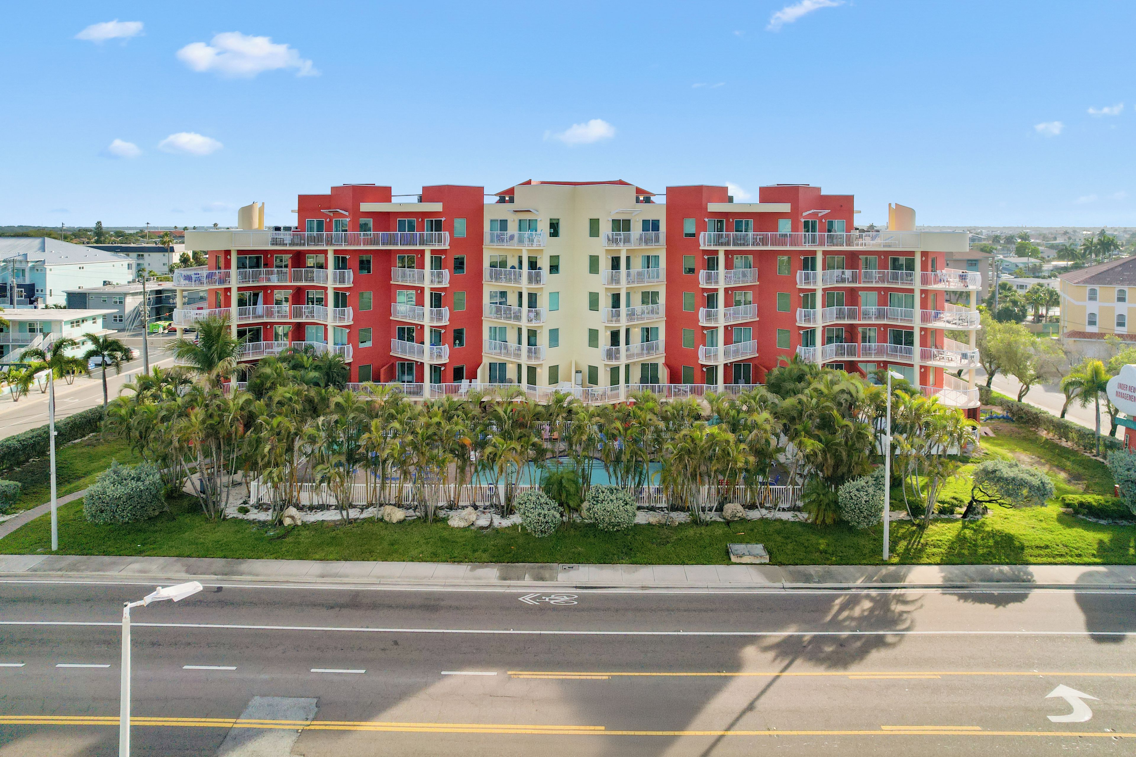A multi-story hotel with balconies, a swimming pool, and a well-maintained garden.