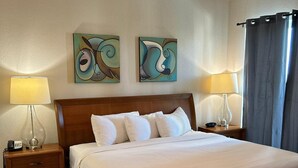 Une chambre d’hôtel avec un lit en bois, deux tables de chevet avec des lampes, un ventilateur de plafond et des œuvres d’art abstraites accrochées au mur.