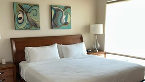 A neatly made bed in a room with a wooden floor, a ceiling fan, and two abstract paintings on the wall.