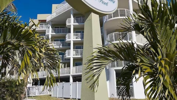 A hotel sign with 'Crystal Palms Beach Resort' written on it, surrounded by palm trees and a building with balconies.