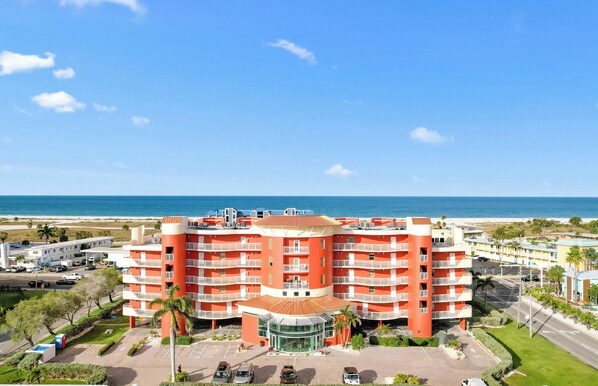 A multi-story hotel with a central courtyard, located near a beach with a clear view of the ocean.
