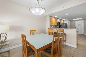 Un comedor con mesa de vidrio y sillas de madera, una cocina con armarios de madera y electrodomésticos de acero inoxidable, y una puerta blanca.