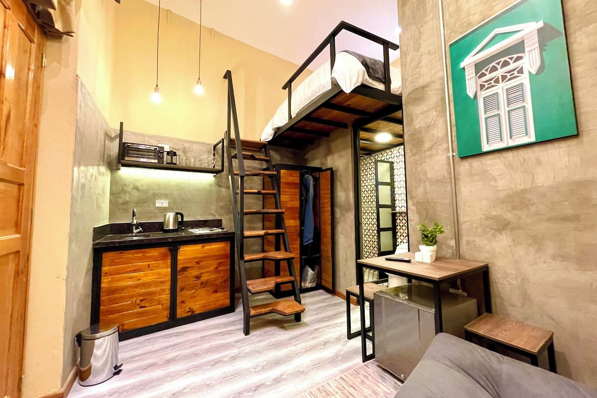 A compact living space with a kitchenette, a lofted sleeping area, a small dining table, and a single potted plant.