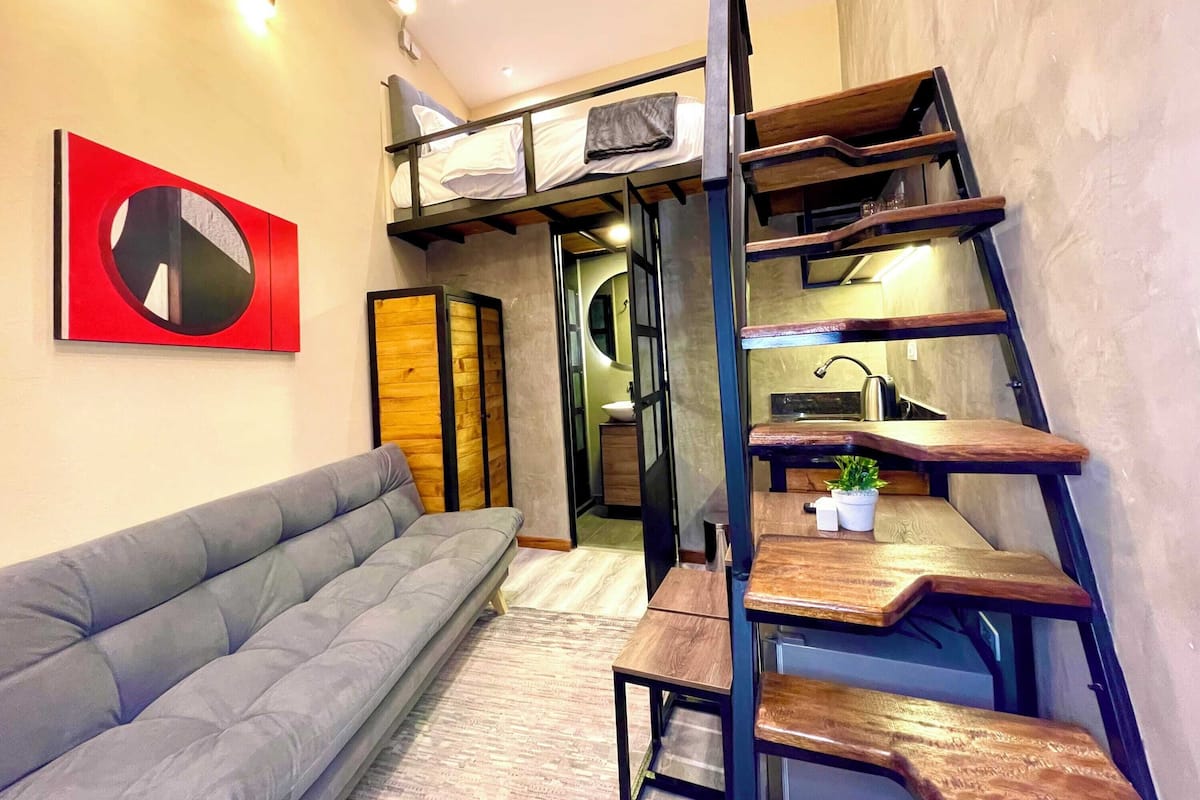 A compact living space with a bunk bed, a sofa, a dining table, and a kitchen area.