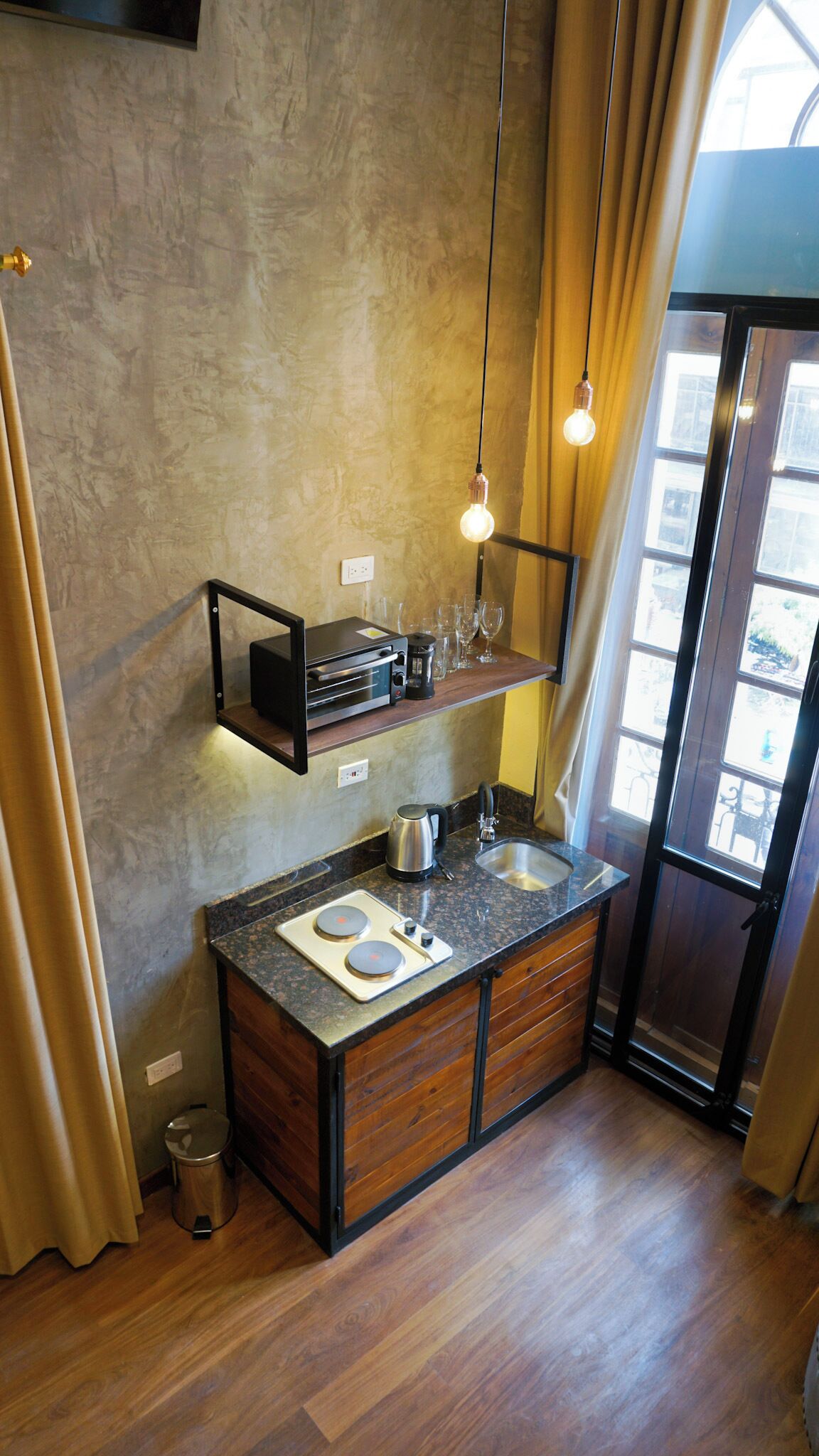 A modern kitchen with a wooden countertop, a built-in oven, a coffee maker, and a hanging light fixture.