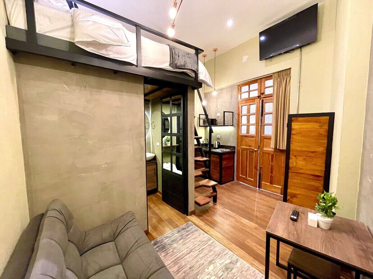 A compact living space with a loft bed, a dining area, and a kitchen.