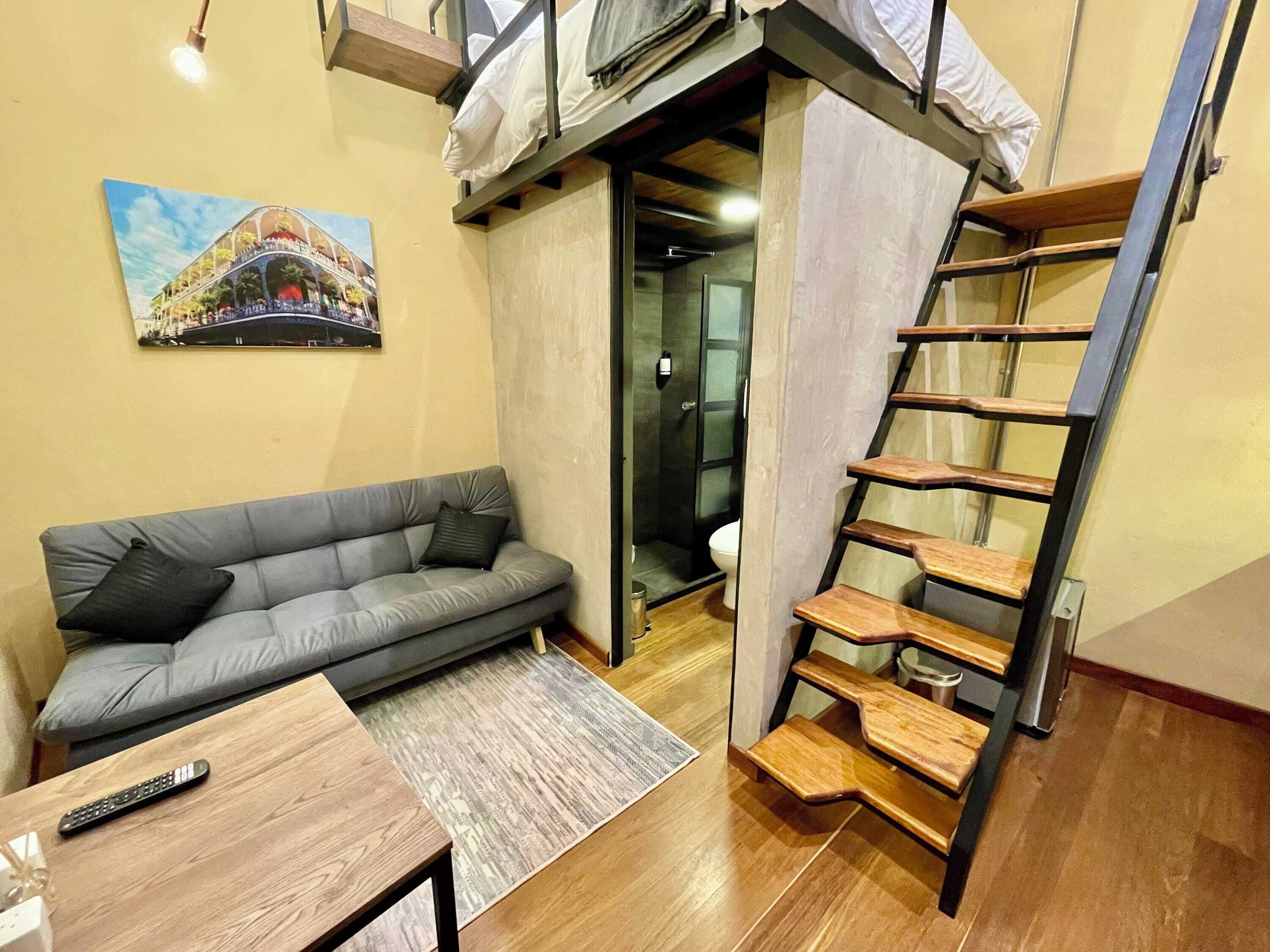 A compact living space with a sofa, a small table, a wooden ladder, and a painting on the wall.