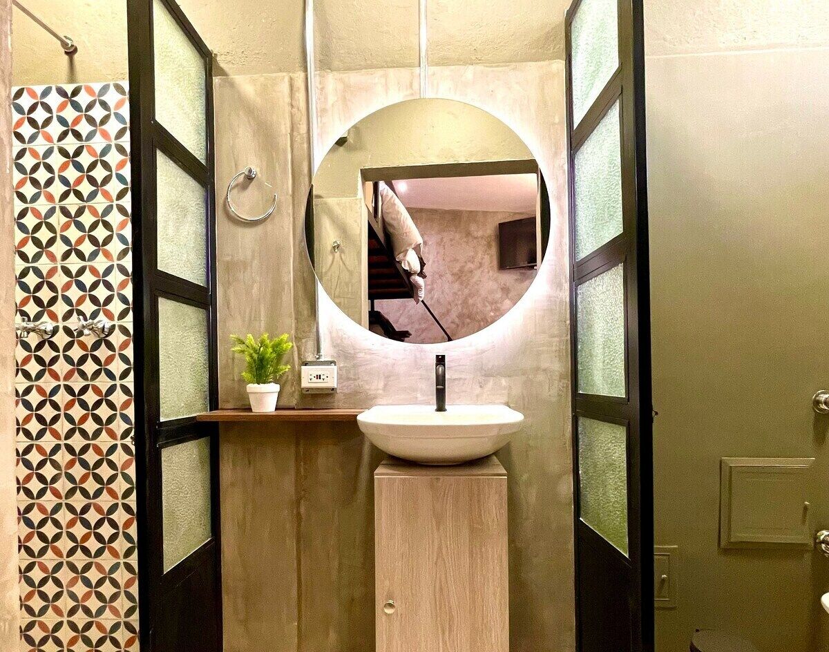 A bathroom with a round mirror, a sink, and a potted plant.