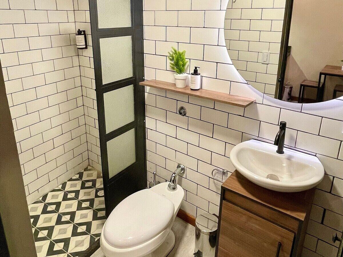 A bathroom with a white toilet, a sink with a mirror above it, and a shelf with toiletries.