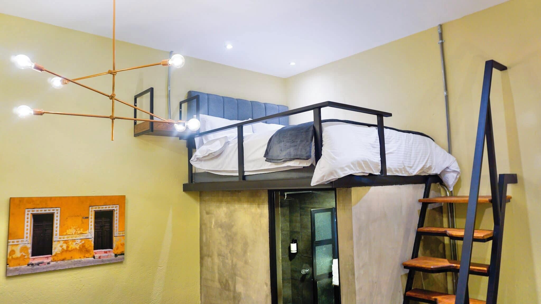 Un dormitorio con literas, una escalera, estante en la pared y una lámpara en el techo.