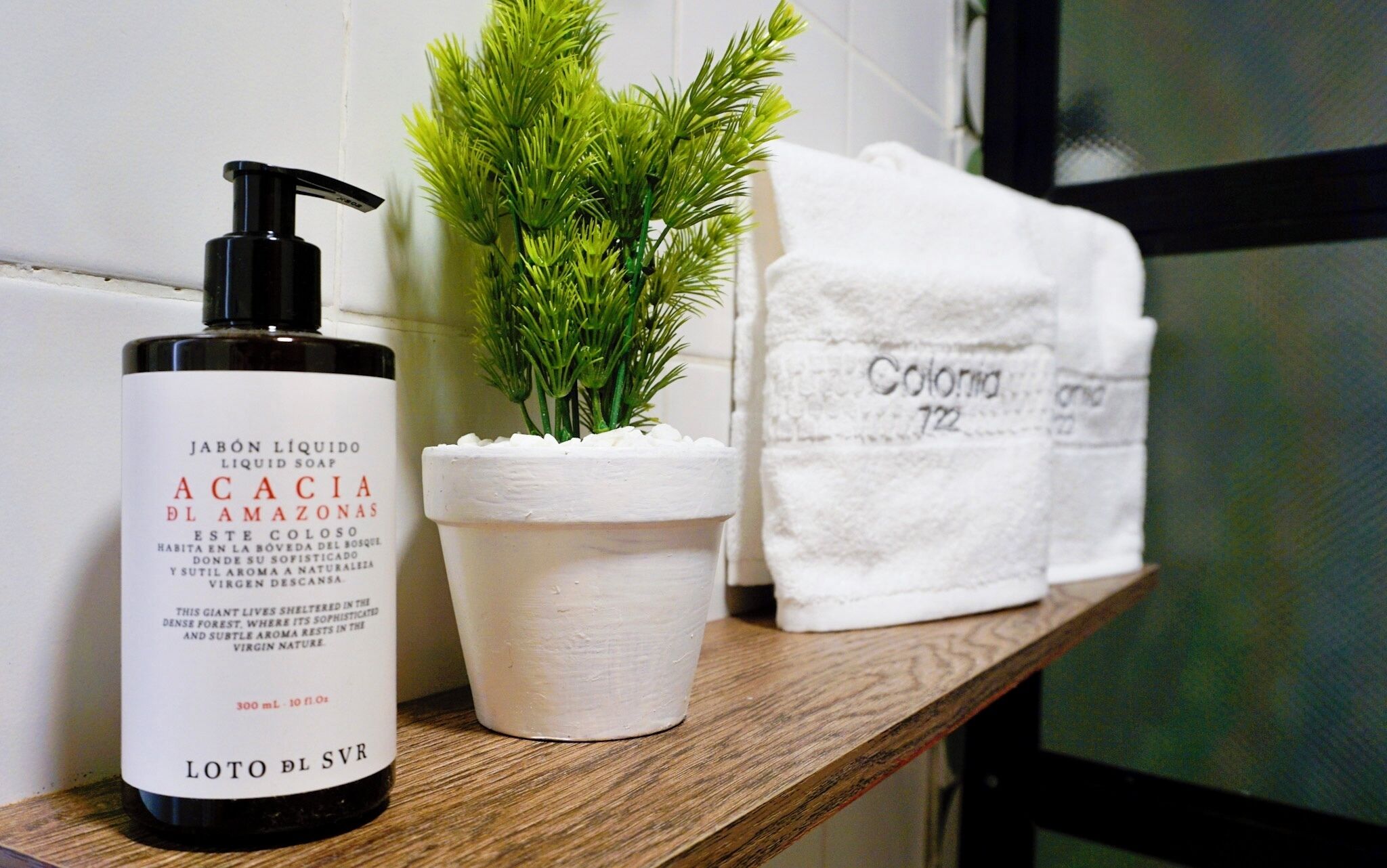 A bottle of liquid soap, a potted plant, and a white towel on a wooden shelf.