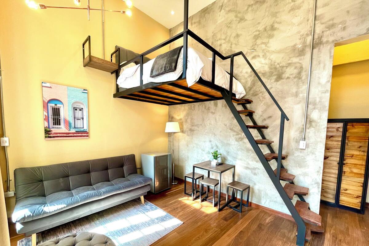 A modern living room with a sofa, a small table, a staircase, and a wall-mounted shelf.