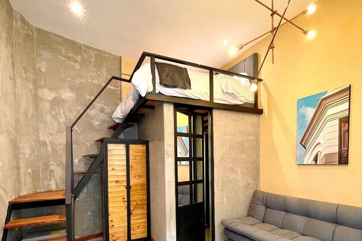 A loft-style room with a bunk bed, a staircase, a sofa, and a painting on the wall.