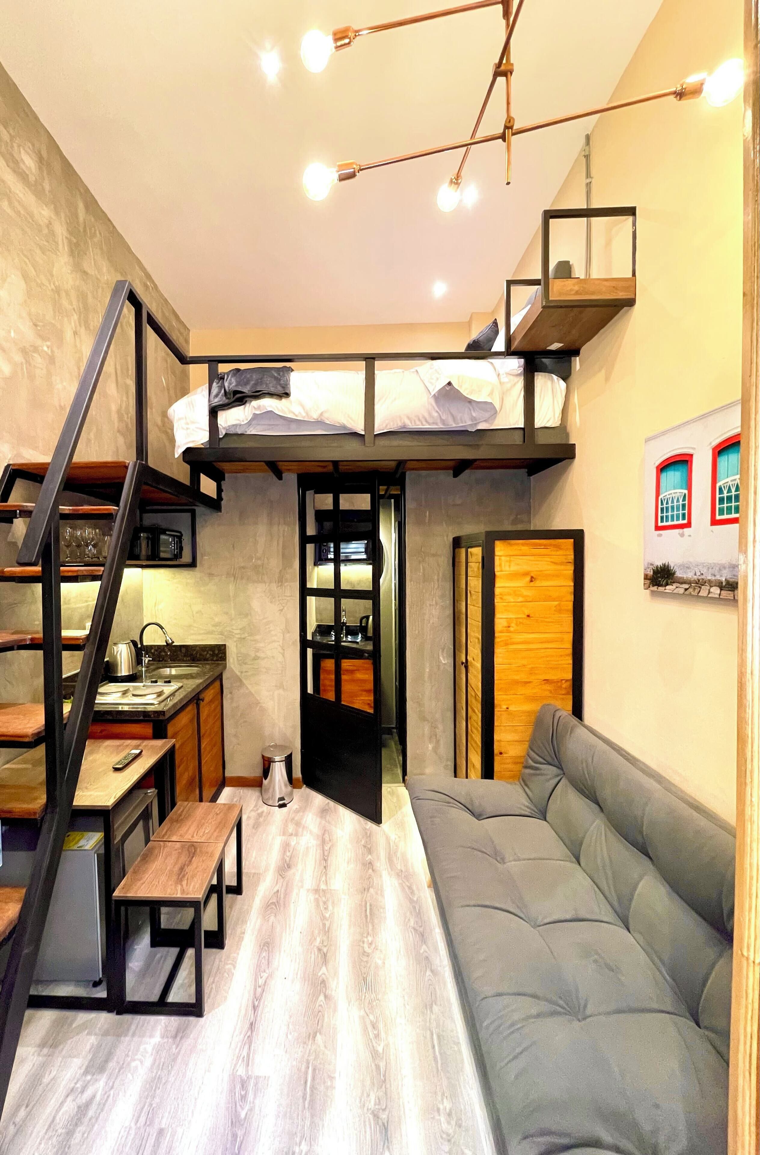 A compact studio apartment with a loft bed, kitchenette, and a sofa.