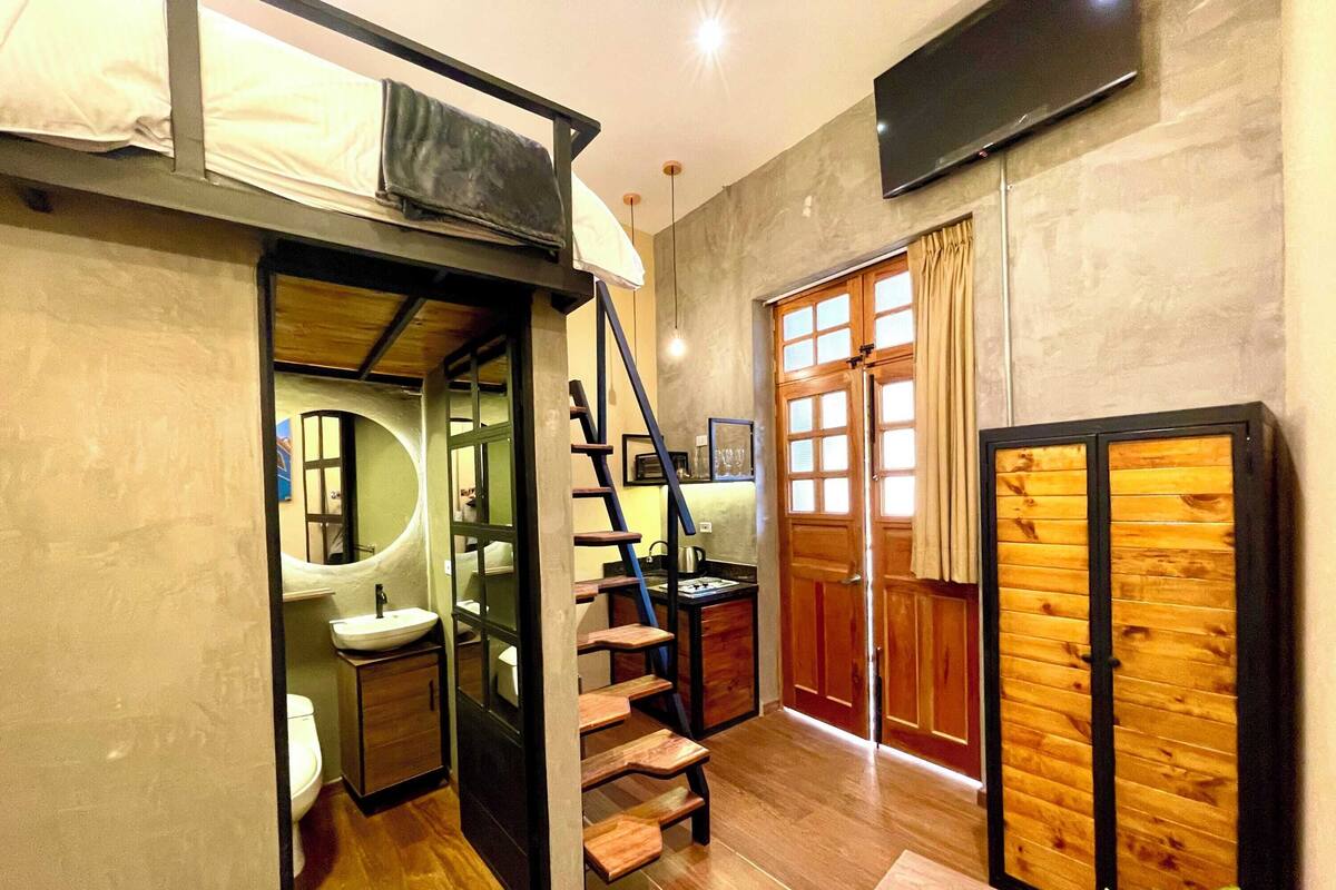 A compact room with a bunk bed, a small bathroom with a sink, a staircase, and a sliding door.