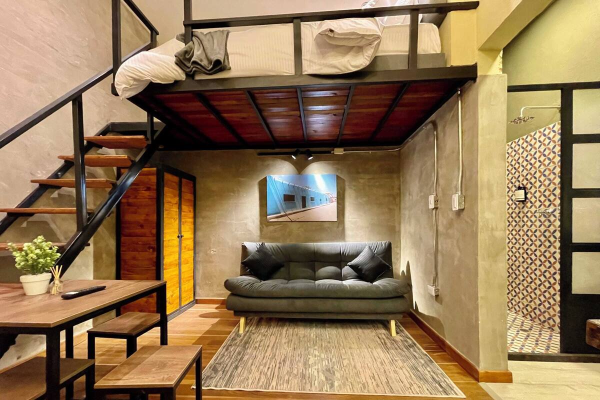 A compact living space with a loft bed, a sofa, a dining table, and a staircase.