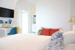 A modern hotel room with a bed, a desk, a chair, and a TV mounted on the wall. - Pezz Pezz Amalfi Coast Suites (Praiano)