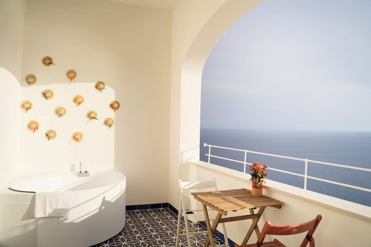 Un baño con bañera, una mesita con una planta en maceta y vista al mar.
