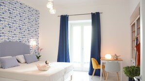 A bedroom with a bed, a desk, and a chair. There is a window with curtains, a plant, and a lamp. - Pezz Pezz Amalfi Coast Suites (Praiano)