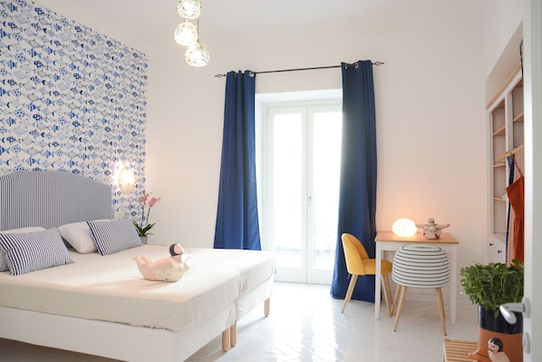 Une chambre à coucher avec un lit, un bureau et une chaise. Il y a une fenêtre avec des rideaux, une plante et une lampe.