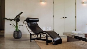 Ein modernes Zimmer mit einem schwarzen Ledersessel, einer Topfpflanze, einer Glastür und einem Tisch mit Büchern.
