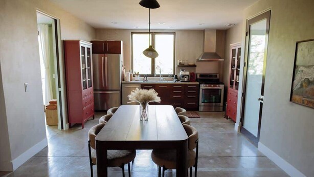 A modern kitchen with a dining area, featuring a large table and chairs, a hanging light fixture, and a view of the outside through a window. - Designer's Apartment in the Heart of West Hollywood (West Hollywood)