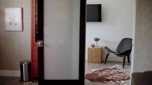 A modern room with a sliding door, a mounted TV, a red cabinet, a small wooden side table, a black chair, and a cowhide rug. - Designer's Apartment in the Heart of West Hollywood (West Hollywood)